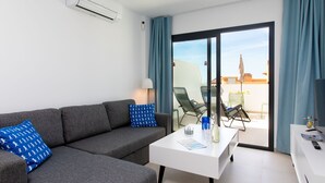 Una sala de estar moderna con un sofá gris, una mesa de centro blanca y un balcón con mobiliario exterior.