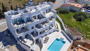 Un edificio blanco de varios pisos con balcones, una piscina en la azotea y un jardín circundante.