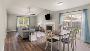 A spacious living room with a fireplace, a dining area with a table and chairs, a sofa, and a television mounted on the wall. - Tipsy Turtle - New Listing (Brunswick)
