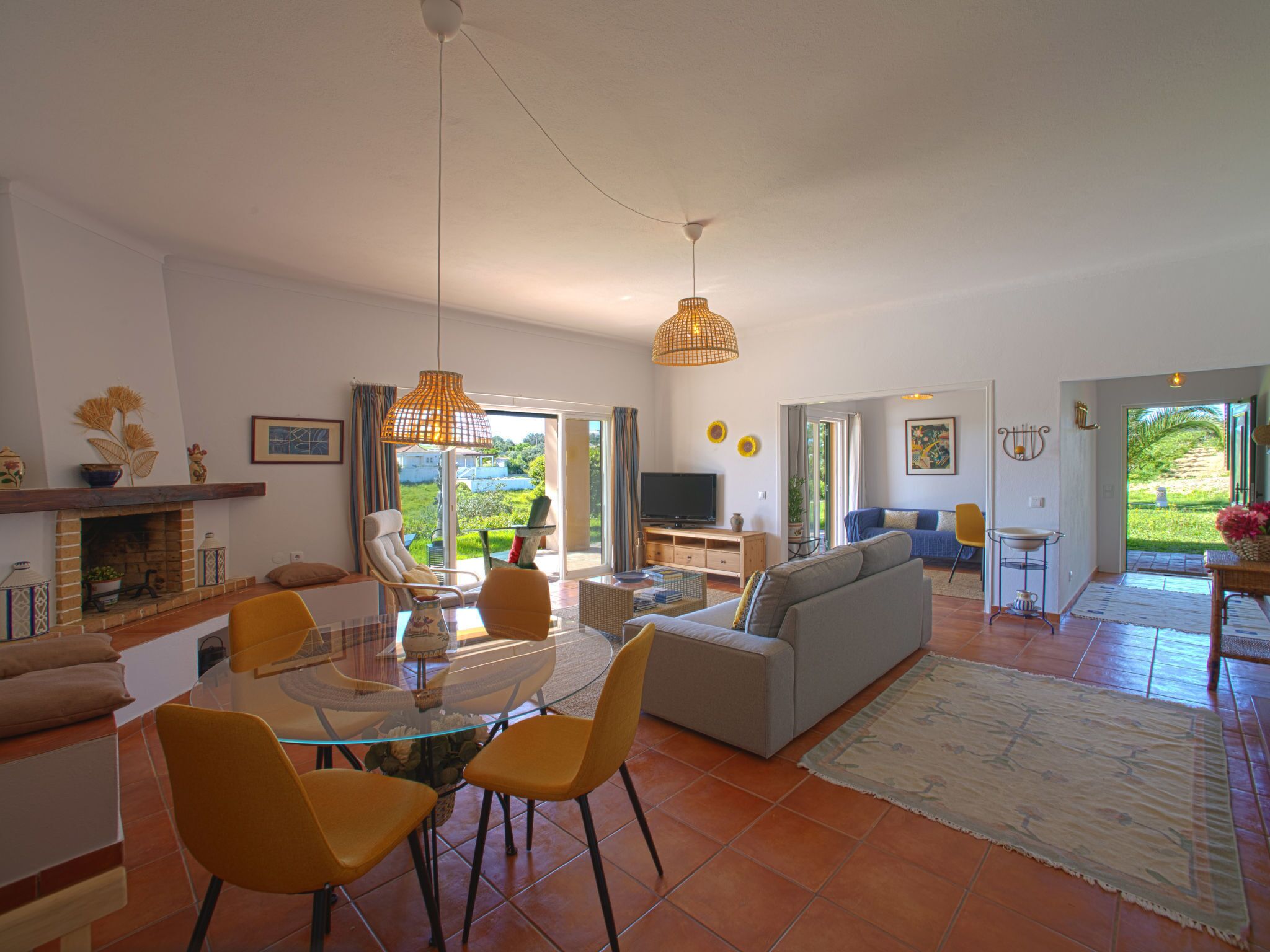A spacious living area with a glass dining table, yellow chairs, a grey sofa, and a TV.