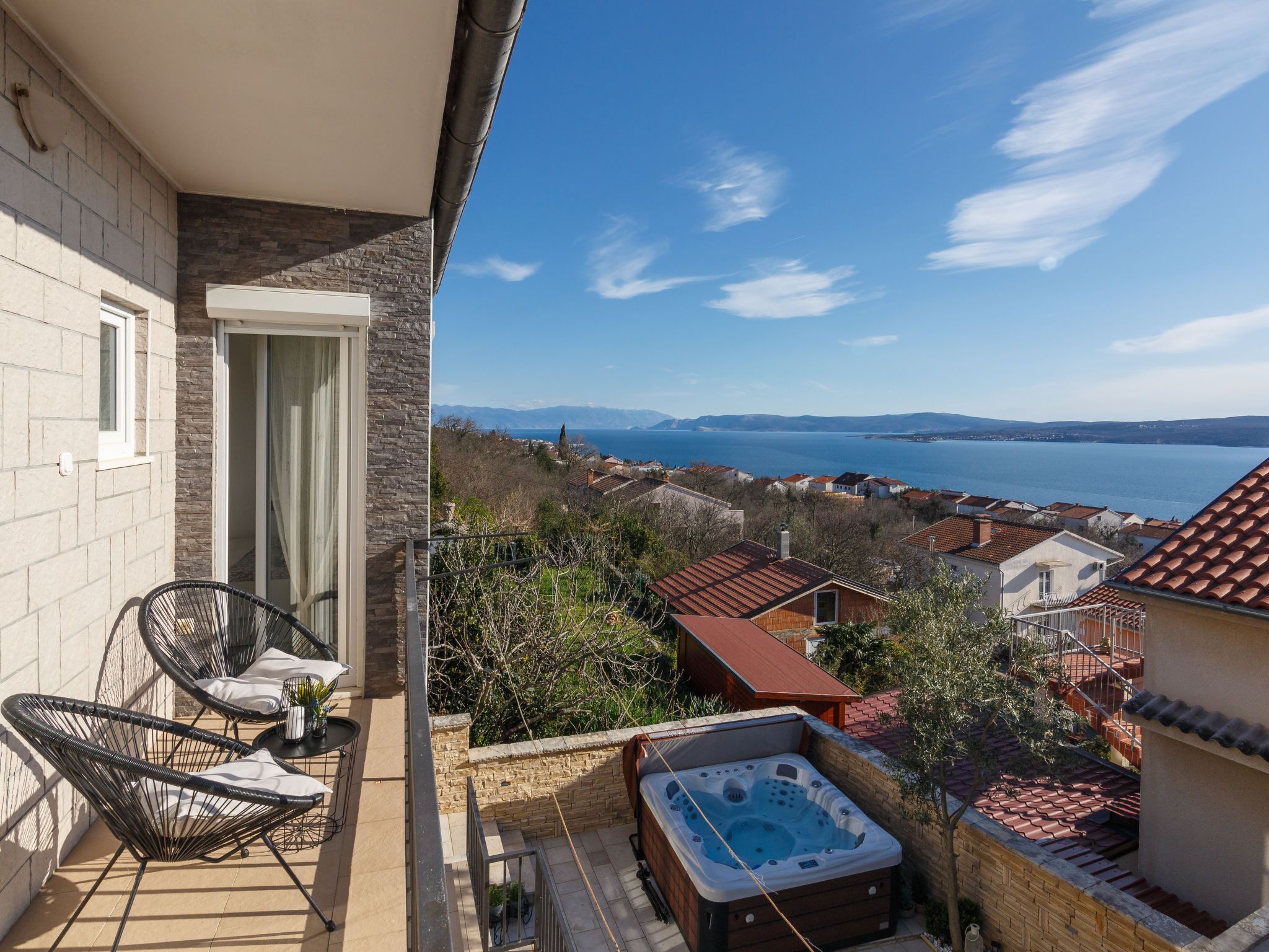 En balkon med jacuzzi, fletstole og udsigt over en sø og bjerge.