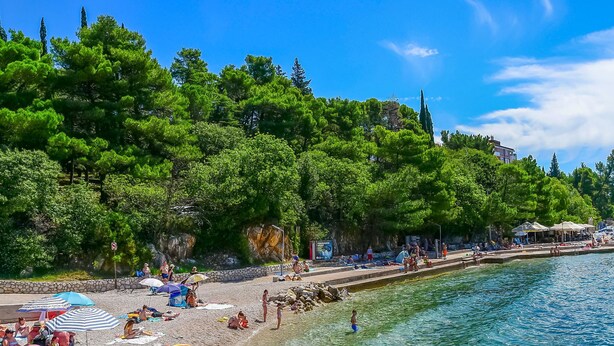 Ein Strand mit klarem Wasser, badenden Personen und Sonnenschirmen.