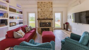 Una sala de estar con chimenea de piedra, un sofá rojo, sillones azul turquesa y una estantería llena de libros y objetos decorativos.