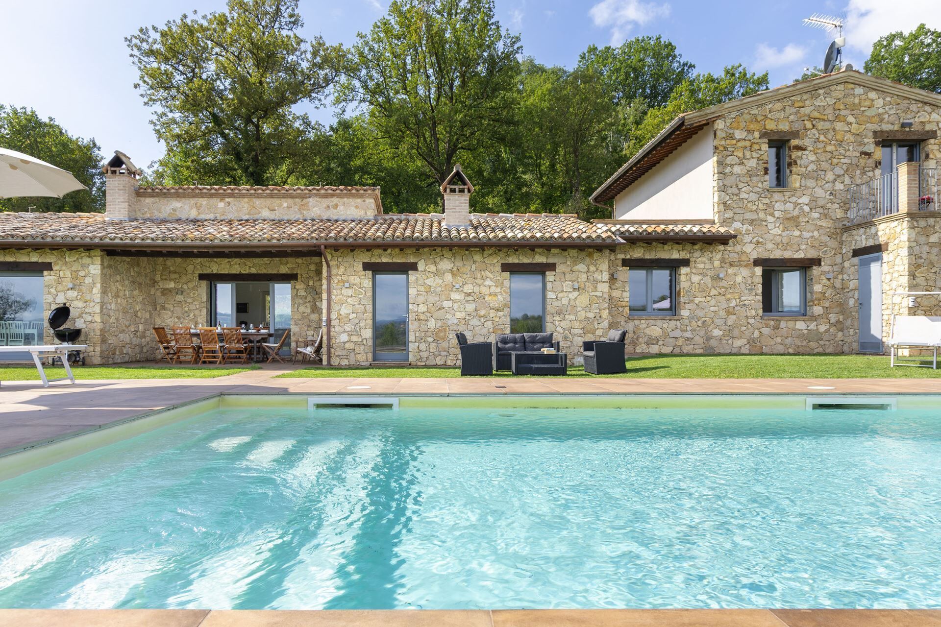 Ein Steinhaus mit Schwimmbad, Außenbereich zum Sitzen und Grillplatz.