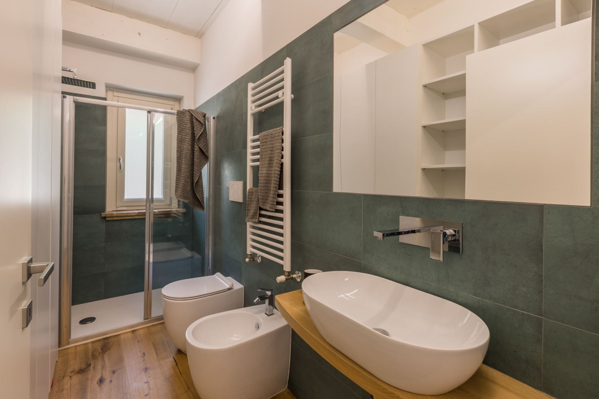A bathroom with a glass shower enclosure, two toilets, a large sink, and a towel rack.