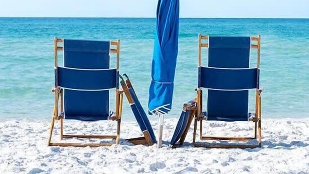 Deux chaises de plage avec des serviettes bleues, sur une plage de sable, avec une mer bleue et limpide en arrière-plan.