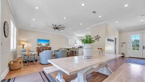 Un vaste espace de vie comprenant une grande table en bois, des canapés bleu clair et un ventilateur de plafond.