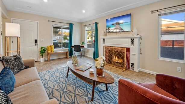A living room with a sofa, a red armchair, a coffee table, a fireplace, and a painting of a beach scene.