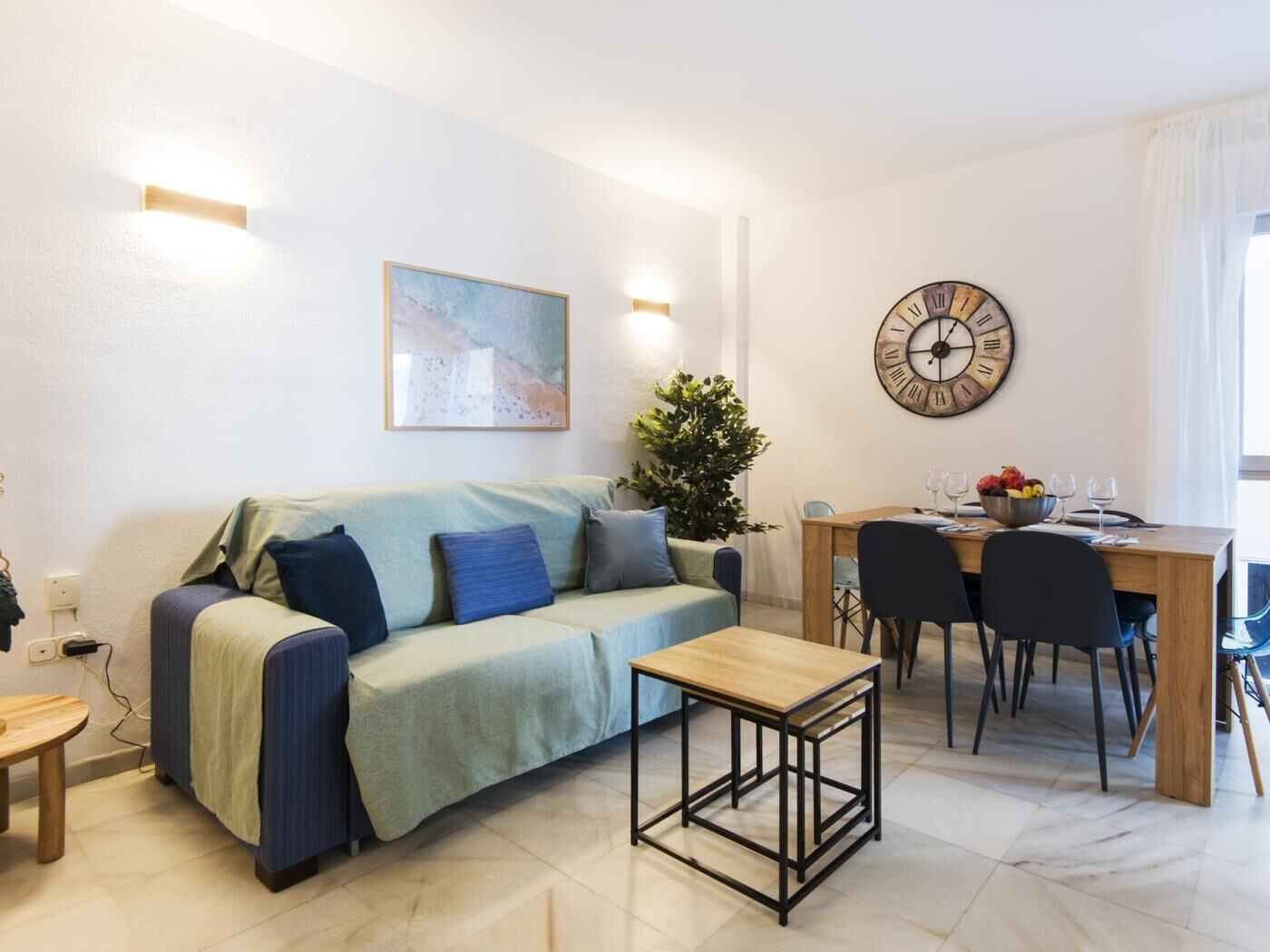 Una sala de estar moderna con un sofá, una mesa de centro, una mesa de comedor con sillas, un reloj y una planta.