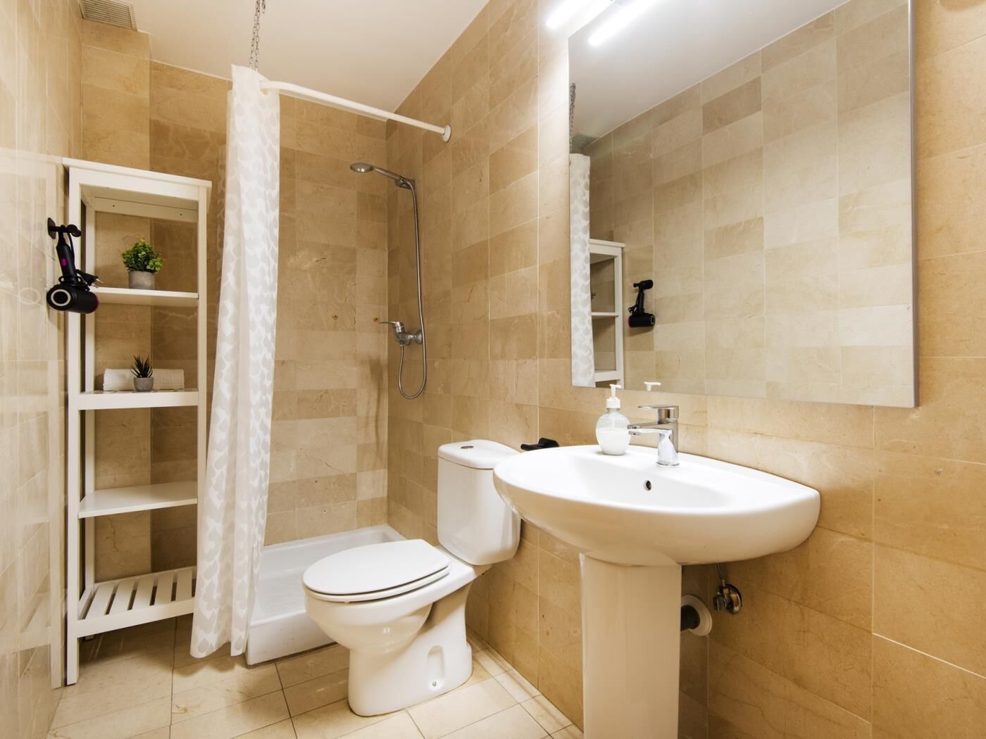 Une salle de bain équipée de toilettes, d’un lavabo, d’une douche et d’une étagère où sont rangés les articles de toilette.