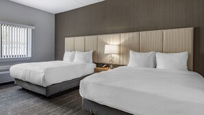 Una habitación de hotel con dos camas, un cabecero de madera, una mesita de noche con lámpara y una ventana con persianas.