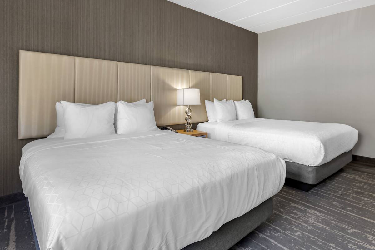A hotel room with two beds, a headboard, a bedside table with a lamp, and a modern design.