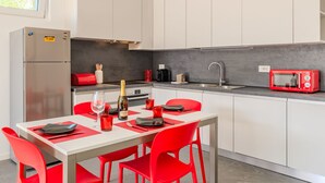 A modern kitchen with white cabinets, a red microwave, and a dining area with red chairs and a table set for two. - Sunny House by Interhome (Gravedona)
