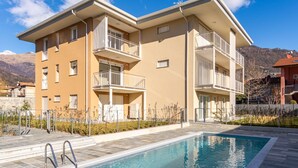 A modern apartment building with a swimming pool, balconies, and a mountain backdrop. - Sunny House by Interhome (Gravedona)