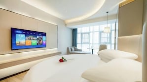 Una habitación de hotel moderna con una televisión de pantalla plana grande montada en la pared, una cama cómoda, una mesita pequeña y una ventana con cortinas.