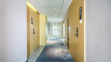 Un pasillo de hotel con puertas a ambos lados, suelo alfombrado y pared de color claro.