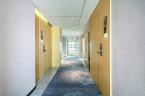 A hotel hallway with doors on both sides, a carpeted floor, and a light-colored wall. - Ou Si Ka lnternational Hotel (Danzhou)
