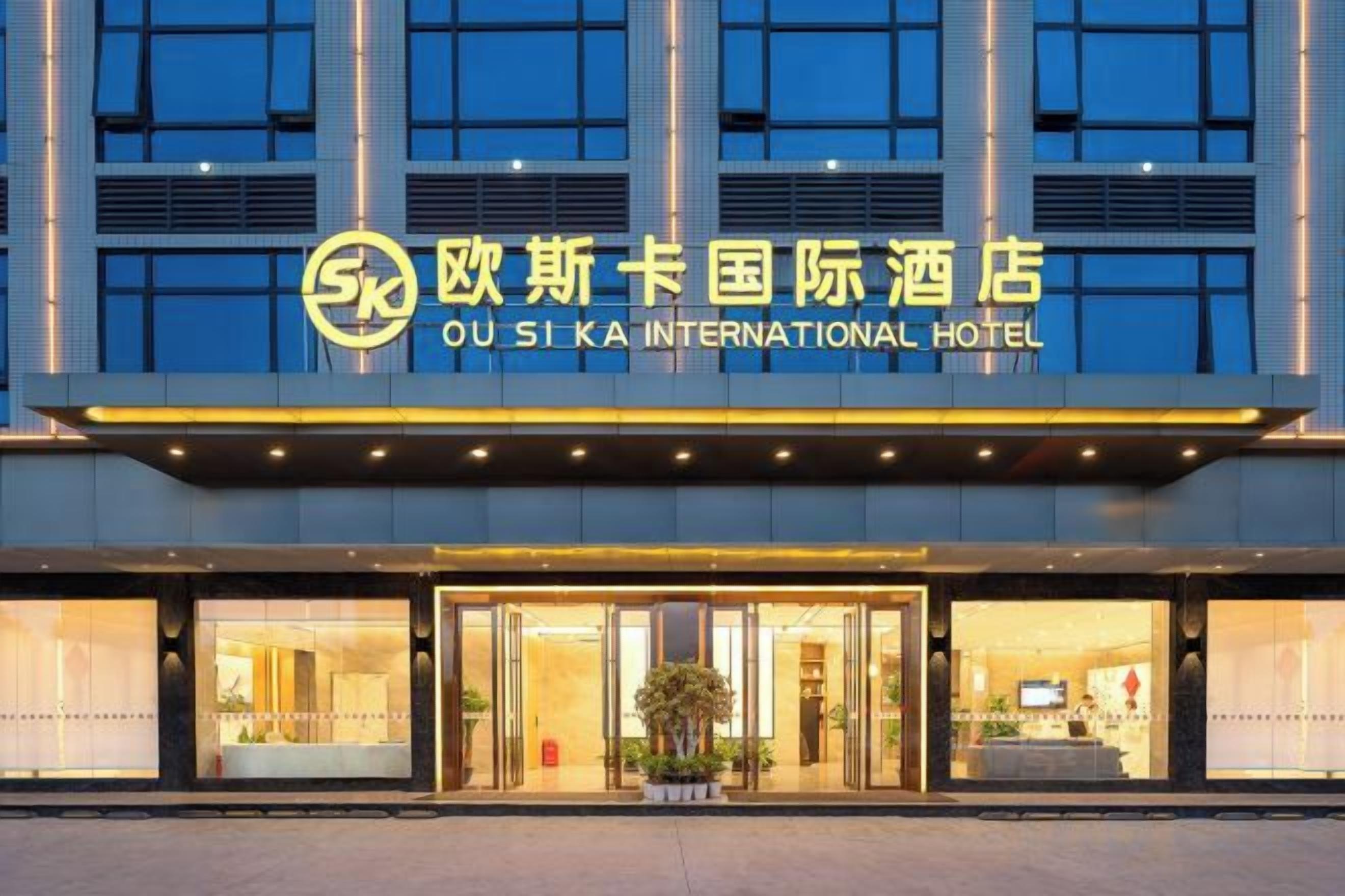 The exterior of the Ou Si Ka International Hotel with a prominent sign, large windows, and a well-lit entrance.