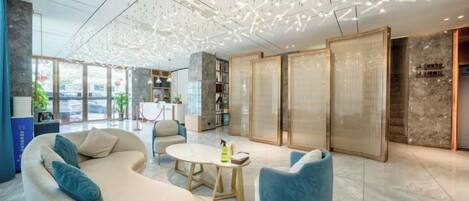 Un vestíbulo moderno con un sofá curvo, una mesa redonda y sillones azules. Hay estanterías y un gran ventanal con vistas.
