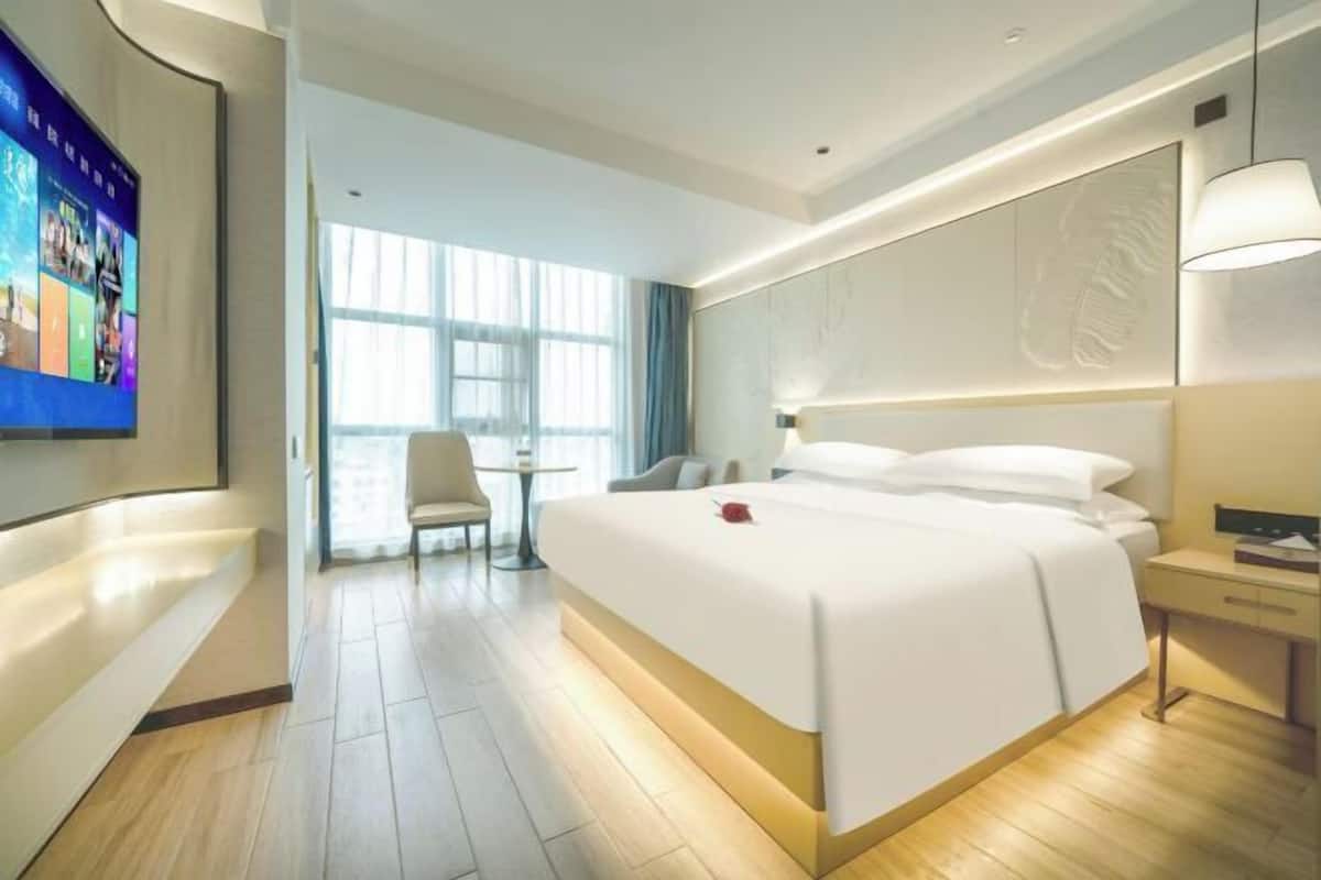 Een moderne hotelkamer met een groot bed, een bureau, een stoel en een televisie die aan de muur is bevestigd.