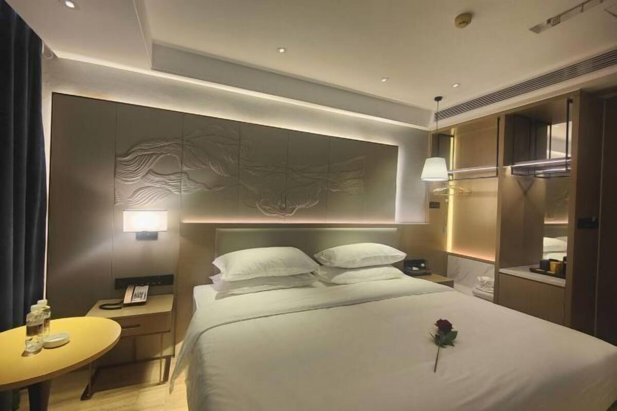 Een hotelkamer met een groot bed, een nachtkastje met een lamp, en een kunstwerk aan de muur.