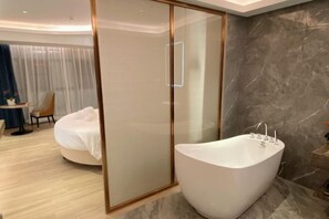 Un bany modern amb una banyera independent, una cabina de dutxa de vidre i una paret de marbre.