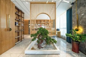 A hotel lobby with a wooden reception desk, a large potted plant, and a bookshelf. - Ou Si Ka lnternational Hotel (Danzhou)