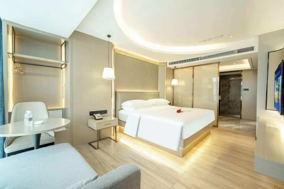 Een moderne hotelkamer met een bed, nachtkastje, lamp en een zithoekje.