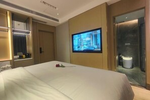 Una habitació d'hotel amb un llit, una televisió penjada a la paret i un bany visible a través d'una porta oberta.
