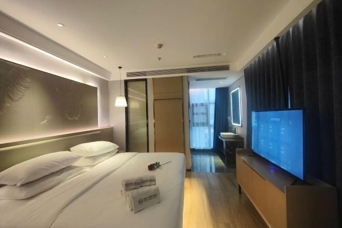 Habitació d'hotel moderna amb un llit gran, televisió de pantalla plana, taulell de nit de fusta i vista al passadís.