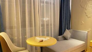 A modern hotel room with a sofa, a chair, a small round table, and sheer curtains.