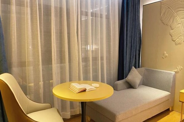 Habitació d'hotel moderna amb un sofà, una cadira, una taula rodona petita i cortines translúcides.