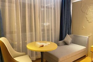 Una habitación de hotel moderna con sofá, una silla, una mesita redonda y cortinas de gasa.