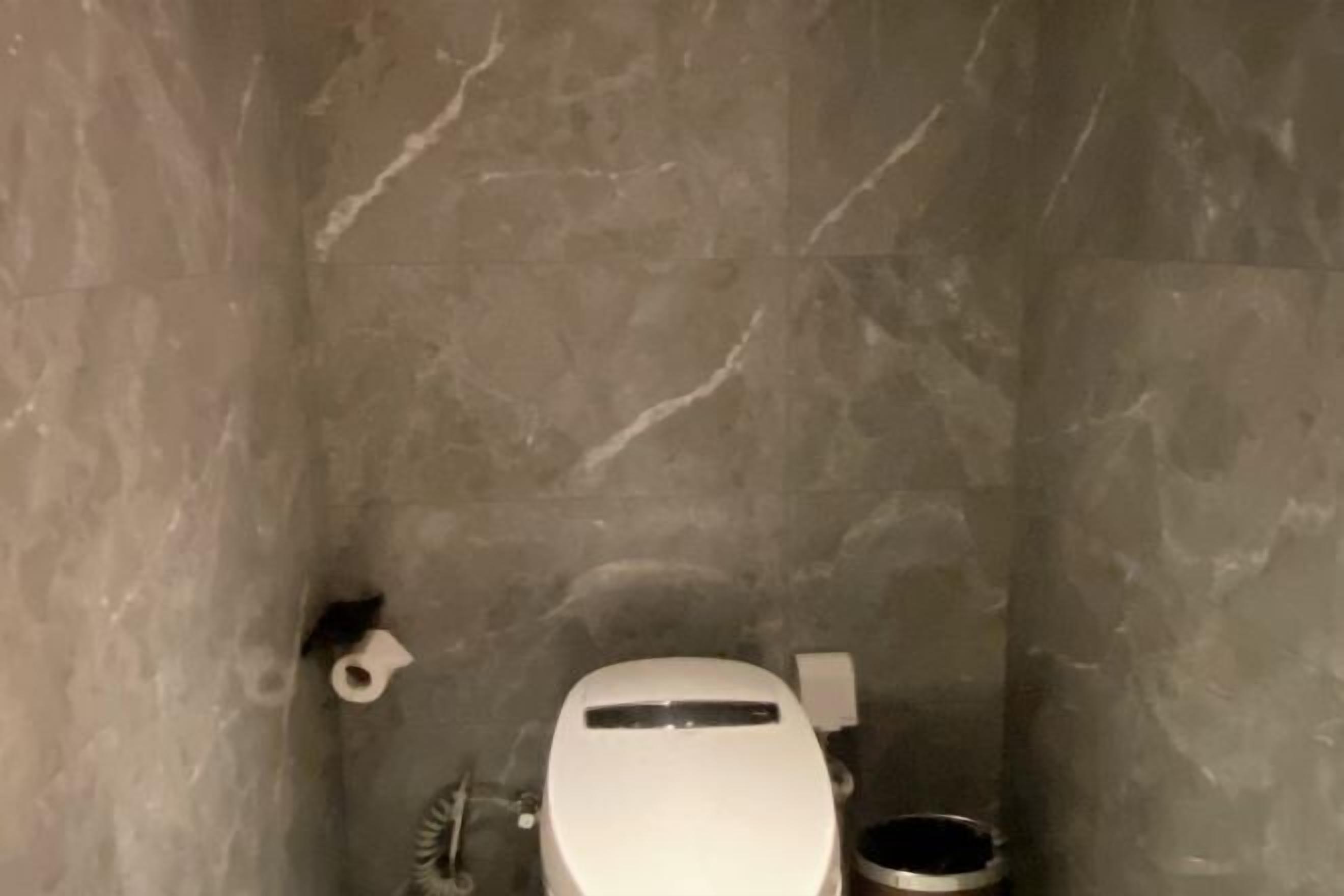 A small, tiled bathroom with a toilet, bidet, and a small trash bin.