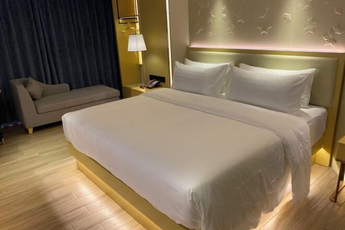 Habitació d'hotel amb un llit gran, un sofà, una taula de nit amb una làmpada i una paret amb un disseny floral.