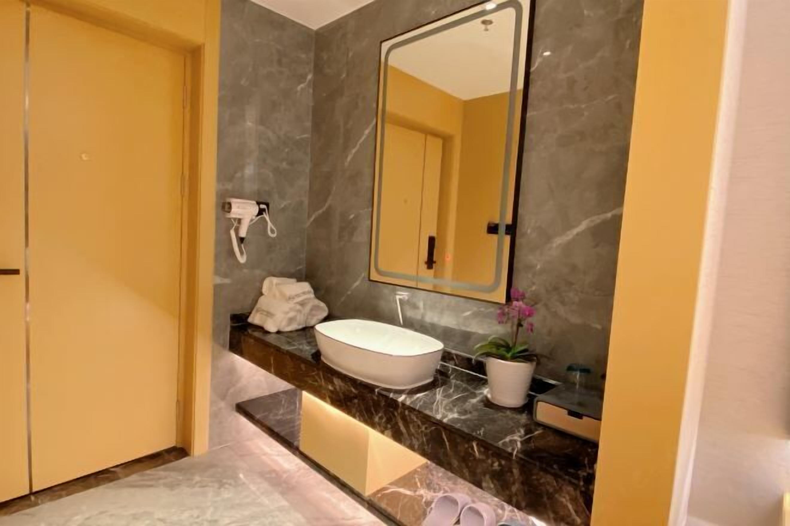 A modern bathroom with a marble vanity, a large mirror, and a potted plant.