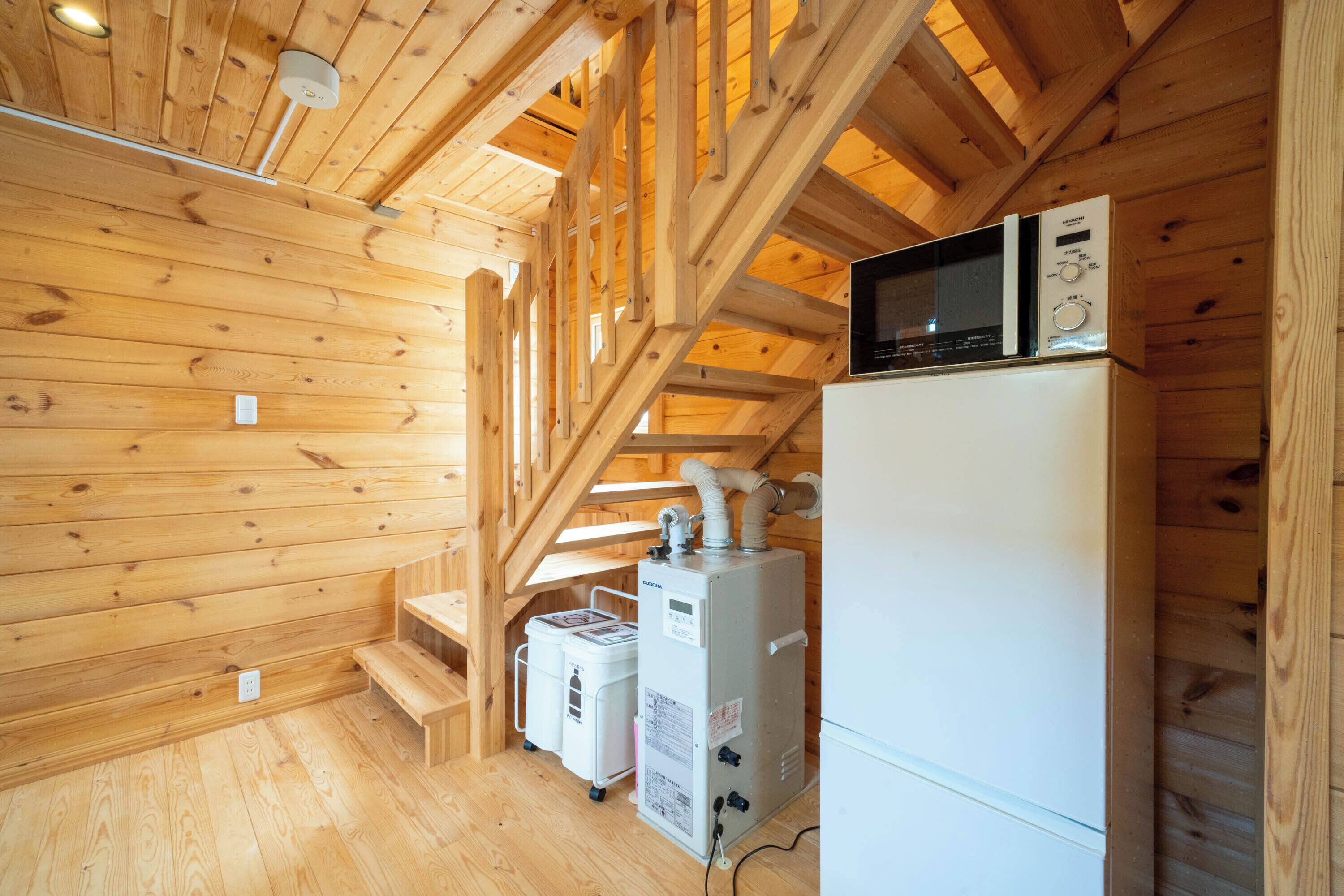 L’intérieur d’une cabane en bois est doté d’un escalier en bois, d’un réfrigérateur blanc, d’un four à micro-ondes et d’un chauffe-eau.