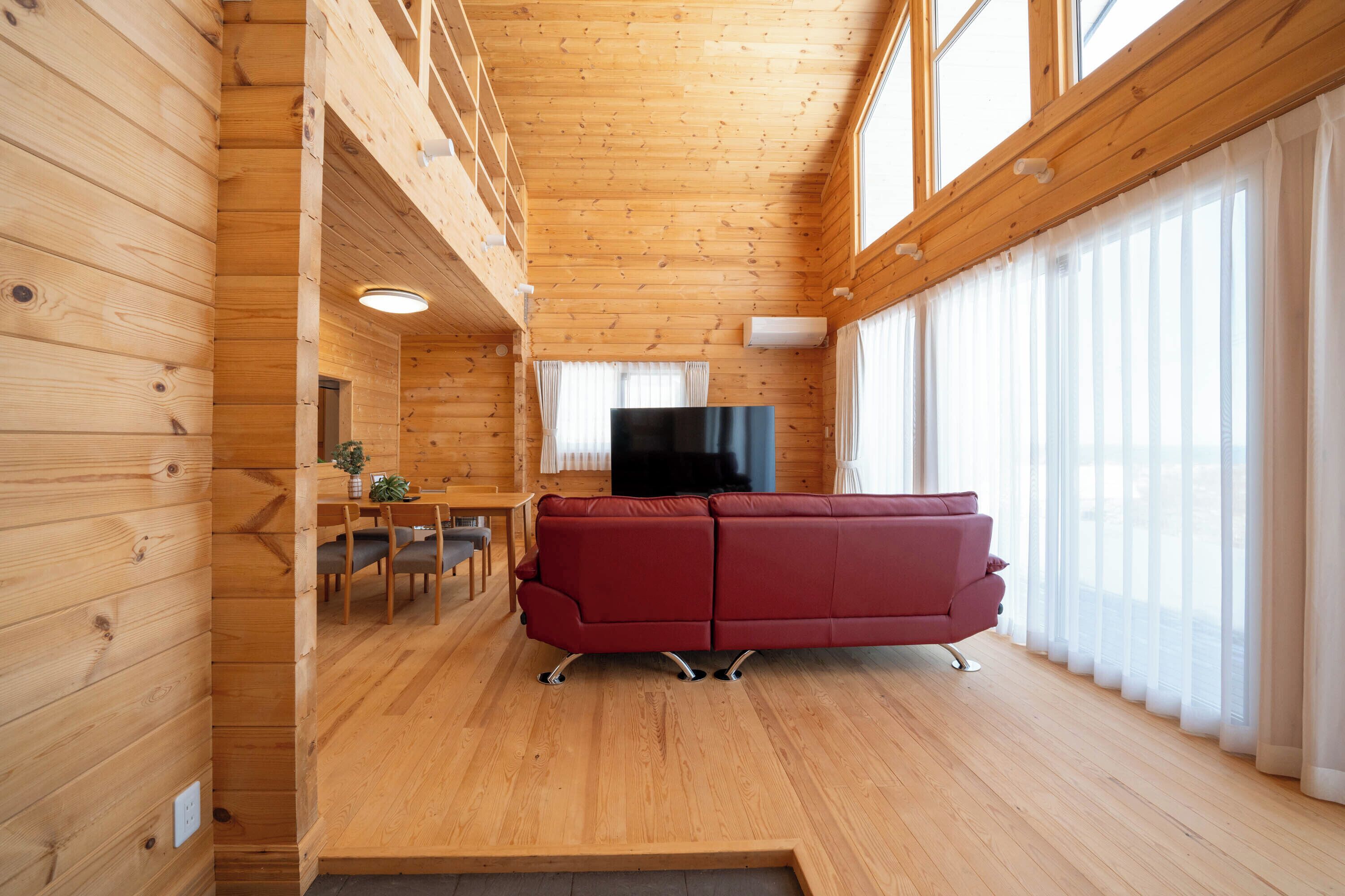 A wooden interior with a red sofa, wooden flooring, and large windows.