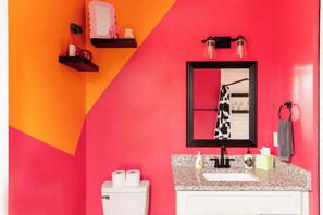 A bathroom with a red and orange color scheme, a sink with a mirror, a towel ring, and a toilet with toilet paper.