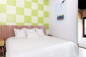 A bed with white bedding, a pink headboard, and a checkered wall pattern.