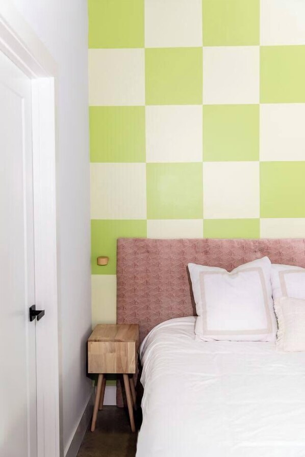 A bedroom with a checkered green and white wall, a pink headboard, and a small wooden nightstand.