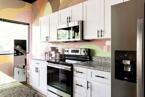 A modern kitchen with white cabinets, a stainless steel stove, a microwave, and a refrigerator.