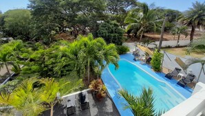 A pool area with lounge chairs and a view of surrounding trees. - Villa Osumare (Flic-en-Flac)
