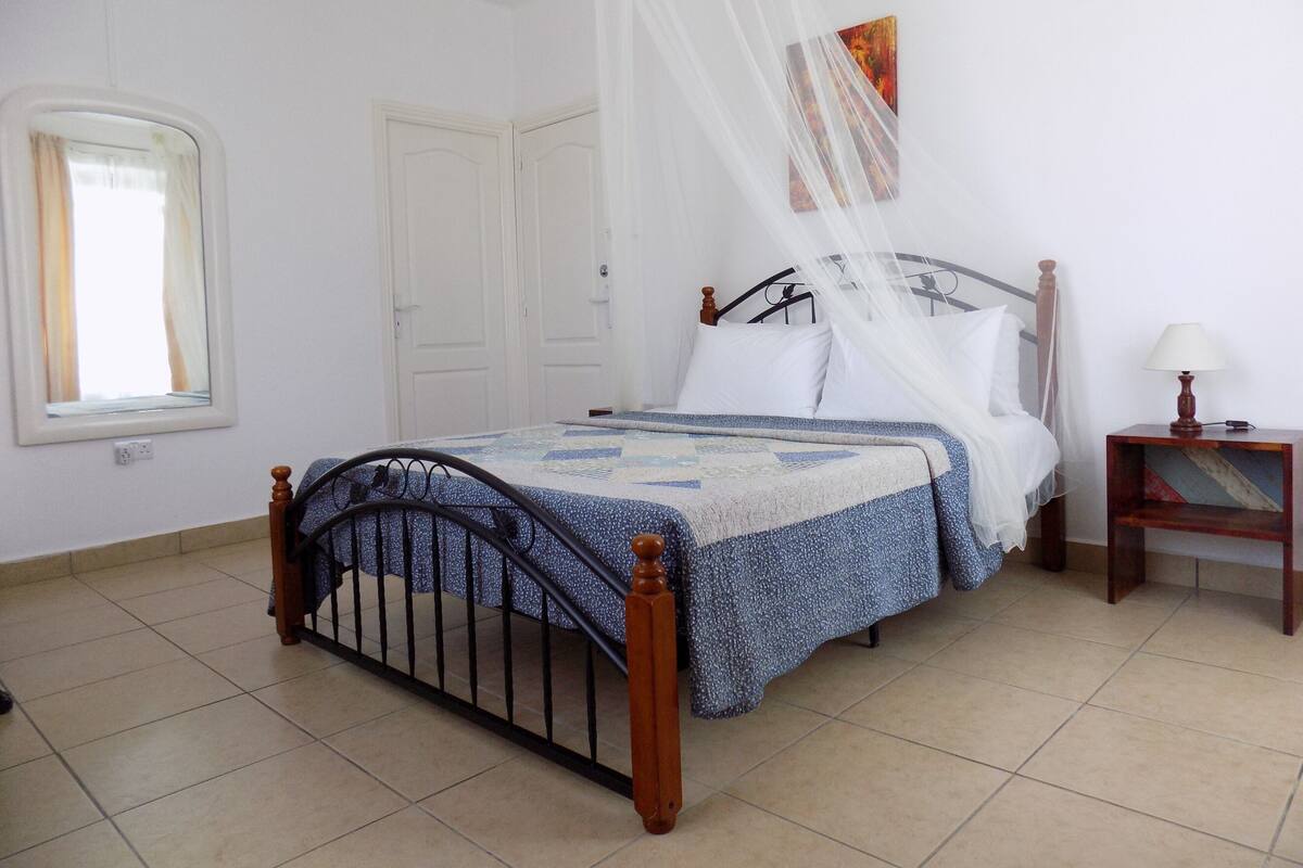 A bedroom with a bed, a nightstand, a lamp, a window with curtains, and a door.