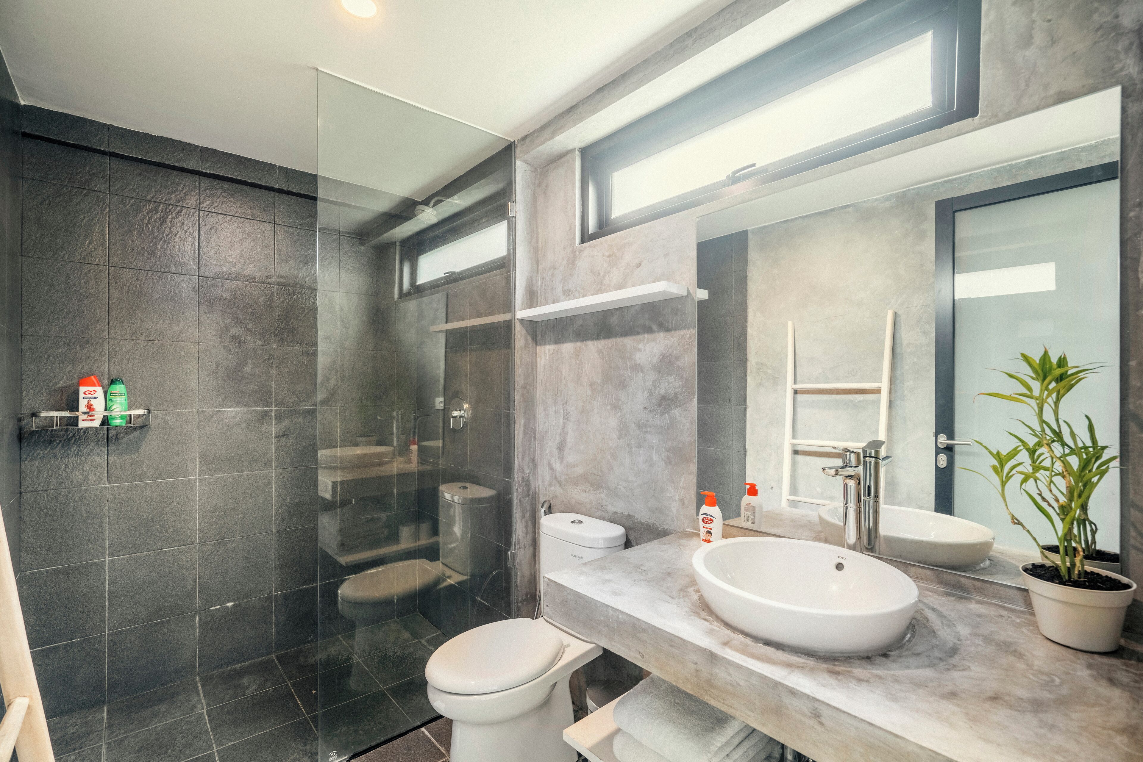 A modern bathroom with a glass-enclosed shower, a white toilet, a large sink, and a mirror.