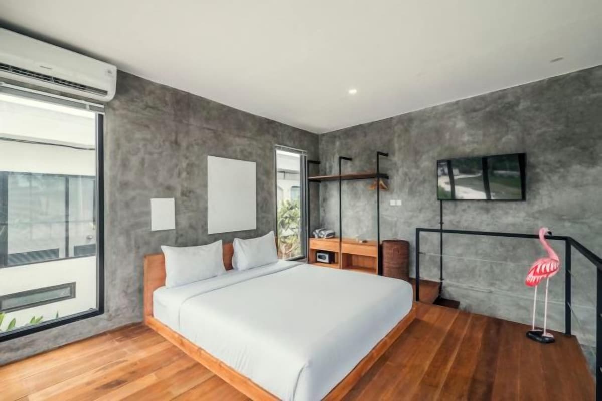 Un dormitorio moderno con una cama grande, un televisor montado en la pared y un ventanal que proporciona luz natural.
