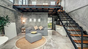 Un espace de vie moderne de style loft, avec un canapé gris, une table basse ronde, un escalier et une grande fenêtre.