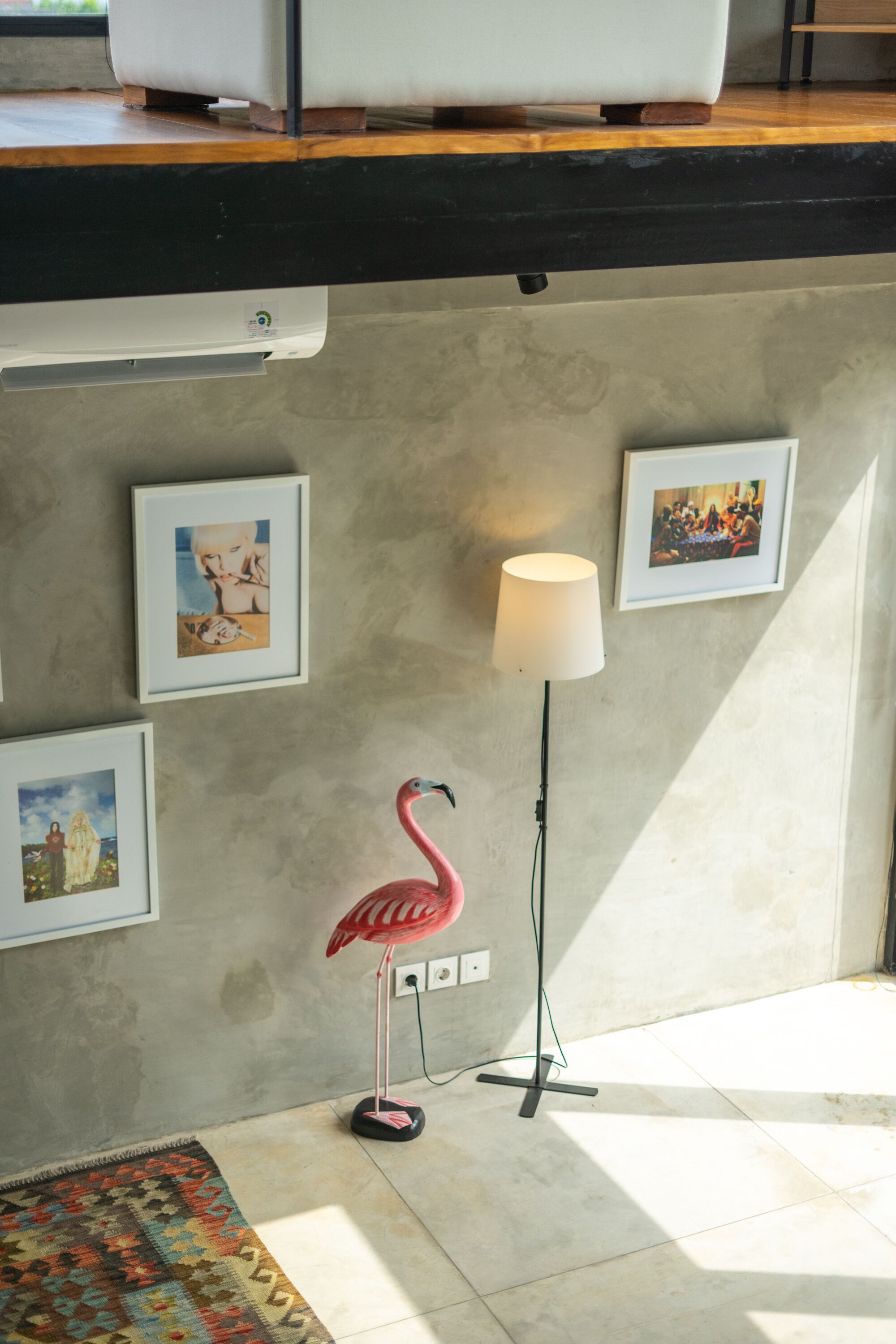 Une pièce avec un mur en béton, un climatiseur blanc, un lampadaire en forme de flamant rose et des tableaux encadrés.