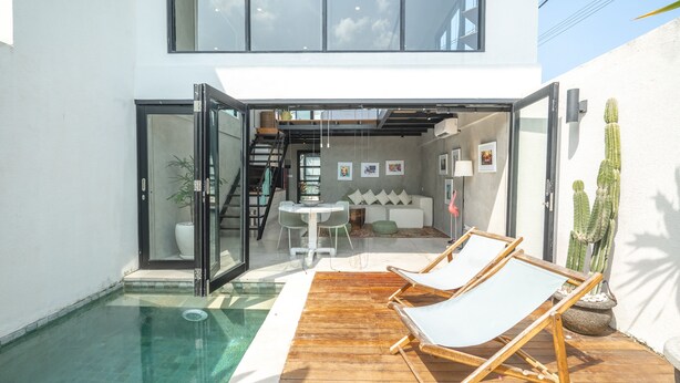 Un espace piscine extérieur moderne, comprenant deux chaises longues, une table à manger et un escalier menant à un niveau supérieur.