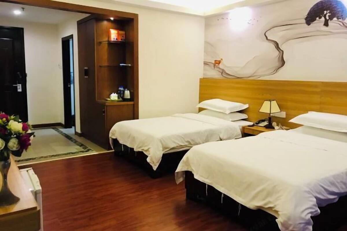Een hotelkamer met twee bedden, een houten hoofdbord, een nachtkastje met een lamp, een houten garderobe en een muurschildering.